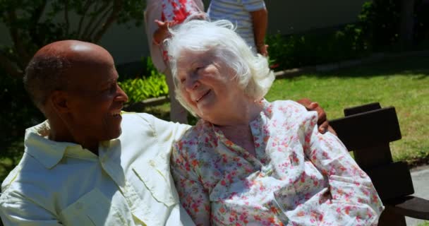在疗养院的花园里 活跃混血的老年夫妇微笑着看着对方 他们坐在长凳上 — 图库视频影像