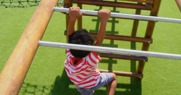 学校の遊び場で水平はしごで遊ぶアフリカ系アメリカ人の男子生徒の高角図 彼ははしご4Kにぶら下がっている — ストック動画