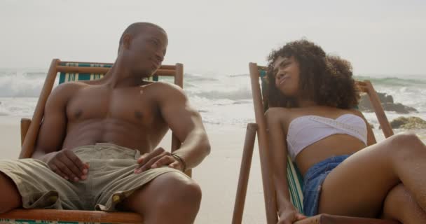 ビーチで交流するアフリカ系アメリカ人カップルの正面図 サンラウンジャー4Kでくつろいでいる — ストック動画