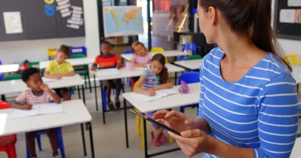 教室でデジタルタブレットを使用して白人女性教師の側面図 教室で勉強する小学生 — ストック動画