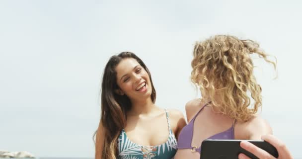 两个混血女性朋友在海滩上用手机自拍的正面景色 他们微笑着 玩得很开心 — 图库视频影像