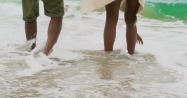 Sahilde deniz dalgaları ile oynayan Afrikalı Amerikalı çift düşük bölümü. Birlikte eğleniyorlar 4k