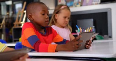 Sınıfta dijital tablet kullanarak Afrikalı Amerikalı öğrencinin ön görünümü. Sınıfta oturan öğrenciler 