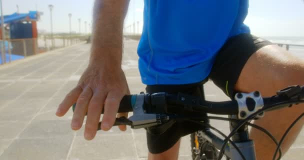 해변에서 산책로에 스마트 워치에 시간을 확인하는 노인의 자전거 4K에 앉아있다 — 비디오