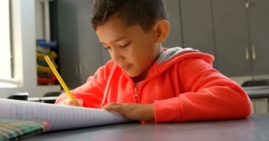 Okulda sınıfta masada okuyan özenli Asyalı öğrencinin ön görünümü. Not defterine yazıyor 4k