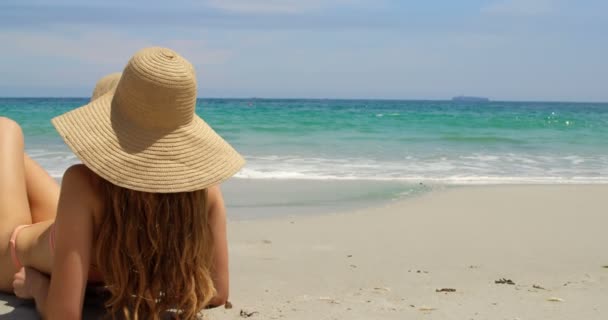 ビーチでくつろぐ帽子をかぶった白人女性の背面 背景に美しい海の波 — ストック動画
