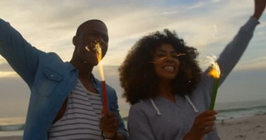 Sahilde elinde kıvılcım tutan Afrikalı-Amerikalı çift düşük açı görünümü. Onlar eğlenceli 4k yaşıyorsanız