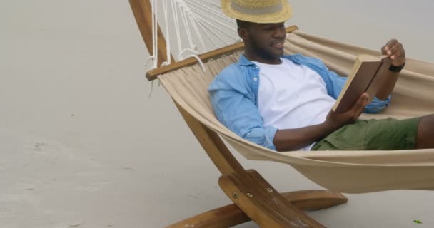 Vista Frontal Del Hombre Afroamericano Leyendo Libro Playa Está Relajando — Vídeo de stock