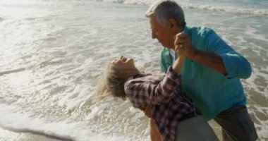 Aktif kıdemli Kafkas çiftinin sahilde birlikte dans ederken ki yan görünümü. Onlar eğlenceli 4k yaşıyorsanız