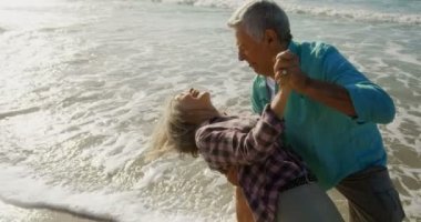 Aktif kıdemli Kafkas çiftinin sahilde birlikte dans ederken ki yan görünümü. Onlar eğlenceli 4k yaşıyorsanız