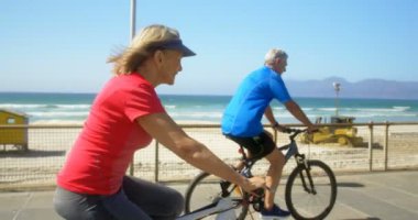 Sahilde bir gezinti üzerinde bisikletsürme aktif üst düzey Kafkas çift yan görünümü. Onlar eğlenceli 4k yaşıyorsanız