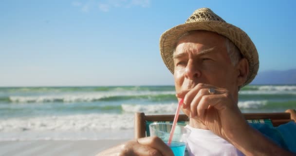 活跃高级白种人在海滩上喝鸡尾酒的正面景色 他在太阳躺椅4K上放松 — 图库视频影像