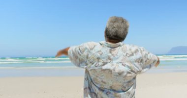 Sahilde ayakta kolları ile aktif üst düzey Afro-Amerikan adam Arka görünümü. Denize bakıyor 4k