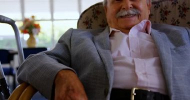 Kafkas kıdemli bir adamın huzurevinde dinlenmesi ön planda. Gülümsüyor ve kameraya bakıyor. 