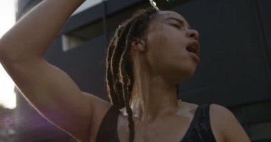Şehirde kafasına su döken genç Afro-Amerikan kadının ön görünümü. O yorgun ve yorgun 4k
