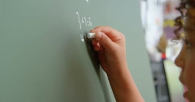 Okuldaki karatahta tahtasında matematik problemi çözen melez bir öğrencinin yan görüntüsü. Toplama yapıyor. 