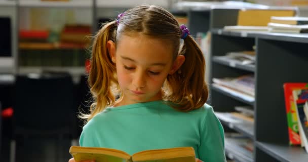 学校で図書館で本を読んでいる丁寧な白人女子高生の正面図 彼女は図書館に立っている4K — ストック動画
