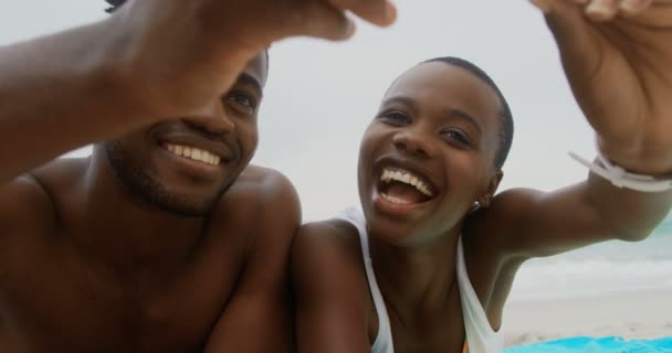 ビーチで携帯電話で自分撮りをするアフリカ系アメリカ人カップルの正面図 ビーチ4Kでくつろいでいる — ストック動画