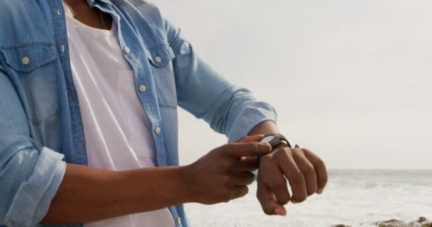 Vista Bajo Ángulo Del Hombre Afroamericano Usando Smartwatch Playa Sonríe — Vídeo de stock