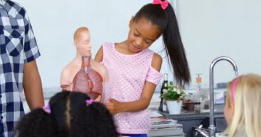 Asyalı liseli kızın sınıfta insan iskeleti modelini açıklarken ön görüntüsü. Erkek öğretmen liseli kızın yanında duruyor. 