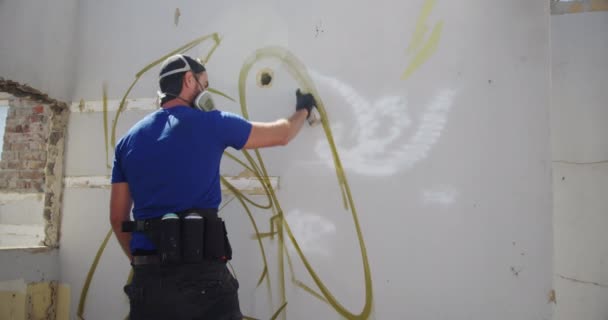 壁にエアロゾルスプレーで描いた白人落書きアーティストの背面図 彼は保護マスク4Kを着用しています — ストック動画