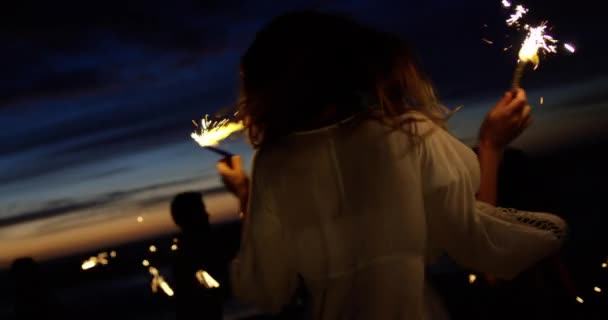 黄昏时分 一群不同朋友在沙滩上玩火花的前方景色 朋友在背景中跳舞 — 图库视频影像