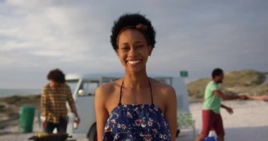 Sahilde bira şişesi ile duran Amerikalı Afrikalı kadın ön görünümü. Arkadaşlar arka planda 4k eğleniyor