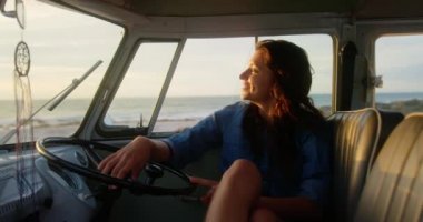 Sahilde karavanda dinlenen Kafkas kadının ön görünümü. O gülümsüyor ve uzağa 4k bakıyor