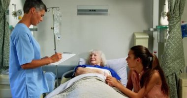 Hastanede ki koğuşta üst düzey hasta ile etkileşimedebilen Kafkas kadın doktorun yan görünümü. Hastane yatağında dinlenen kıdemli hasta 4k