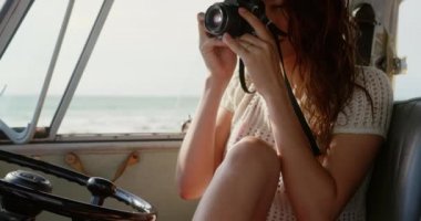 O bir kamp minibüsü 4k otururken dijital kamera ile fotoğraf çeken güzel genç Kafkas kadın ön görünümü