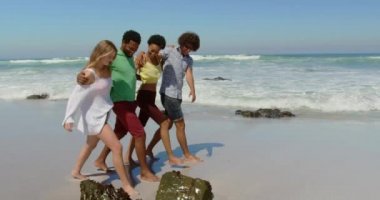 Yürüyüş etrafında kolları ile genç çok etnik arkadaş grubunun yan görünümü ve güneşli bir günde plajda eğlenmek 4k