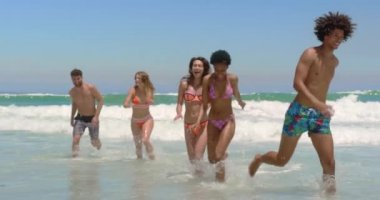 Güneşli bir günde gülümseyip eğlenirken plajda birlikte koşan genç çok ırklı arkadaşların ön görünümü 4k