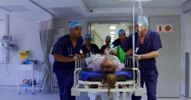Hastanenin koridorunda acil sedye yatağı iten çok ırklı tıbbi ekiplerin ön görüntüsü. 4k