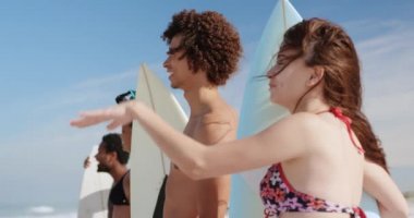 Güneşli 4k plajda sörf tahtaları tutarken çok ırklı genç çok ırklı arkadaşlar birbirleriyle konuşurken grup Yan görünümü