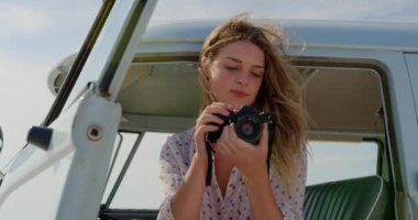 Genç Kafkas kadın plajda karavan dijital kamera fotoğrafları gözden ön görünümü gülümseyerek ve 4k bakarken