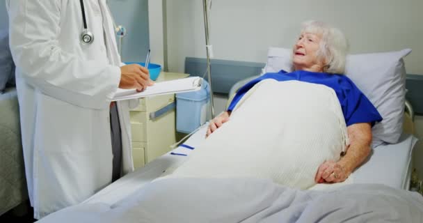 病棟で活動中の高齢者と交流するアジア系男性医師の正面図 クリップボードを保持してる4K — ストック動画