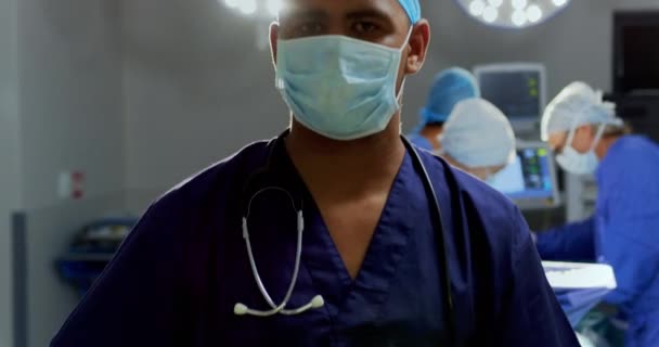Vorderansicht eines afrikanisch-amerikanischen Chirurgen, der im Operationssaal des Krankenhauses steht. Chirurgen operieren im Hintergrund 4k