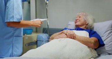 Aktif kıdemli hasta hastanede yatarken beyaz kadın hemşirenin serum serumunu ayarlarken yan görüntüsü. Birbirleriyle etkileşim içindeler.