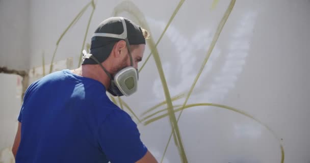 壁にエアロゾルスプレーで描く白人落書きアーティストの側面図 彼は保護マスク4Kを着用しています — ストック動画