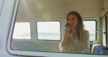 4k uzağa bakarken plajda karavanda cep telefonuyla konuşan genç Kafkas kadının ön görünümü