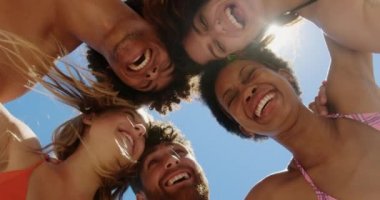 Genç çok etnik arkadaşlar huddle oluşturan düşük açı görünümü ise genç çok etnik arkadaşlar güneş 4k plajda güneş tevekkül ve kamera bakarken huddle oluşturan düşük açı görünümü