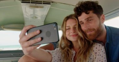 Plaj 4k camper van cep telefonu ile selfie çeken genç Kafkas çift ön görünümü
