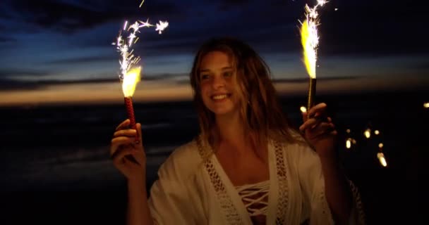 黄昏时分 美丽的白种女人在沙滩上玩火花的正面景色 她微笑着 玩得很开心 — 图库视频影像