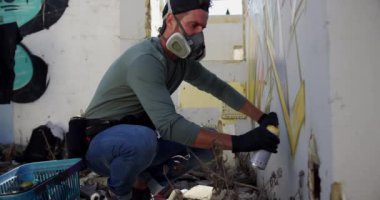 Duvarda aerosol sprey ile kafkas grafiti sanatçısı boyama yan görünümü. O koruyucu maske 4k giyiyor
