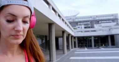 Beyaz kadın sokak dansçısının şehirde kulaklıkla müzik dinlediği ön manzara. O yürüyor ve 4k gülümsüyor