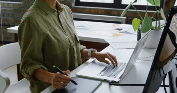 在办公桌上使用图形平板电脑和笔记本电脑的白种女性汽车工程师的侧视图 她坐在4K桌旁 — 图库视频影像