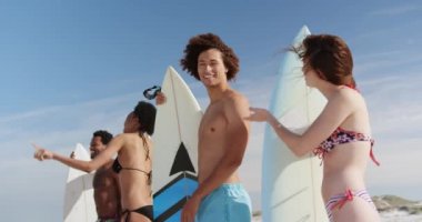 Güneşli 4k plajda sörf tahtaları tutarken birbirleriyle konuşurken genç çok ırklı arkadaşlar çok ırklı grup düşük açı görünümü