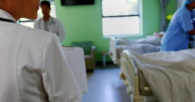 Hastanenin koğuşunda panoya yazı yazan beyaz kadın doktoru. 4K numaralı hastaya bakıyor.