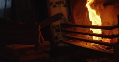Beyaz adamın şömineye tahta kütük koyarak yan görünümü. O şömine 4k yanında oturuyor