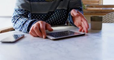 Evde dijital tablet kullanan Beyaz adamın ön görünümü. Masada oturuyor. 4k